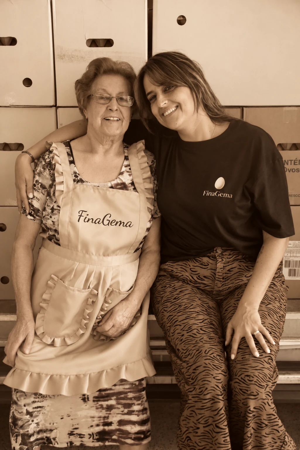Duas mulheres da família FinaGema, abraçadas no armazém, numa fotografia em sépia